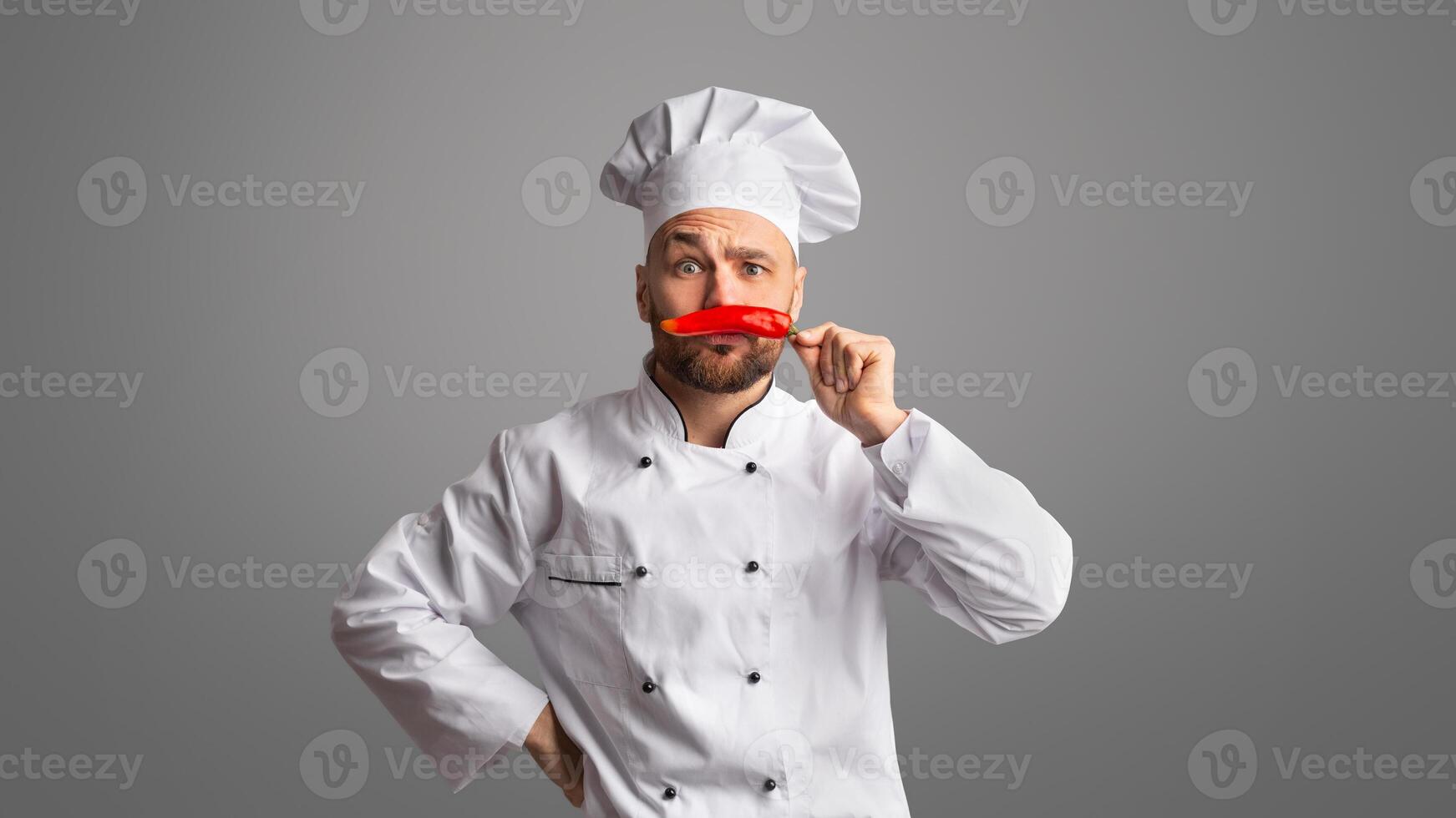 Funny Chef Guy Holding Red Chilli Pepper Near Face Like Moustaches Posing Having Fun Over Black Studio Background. Panorama photo