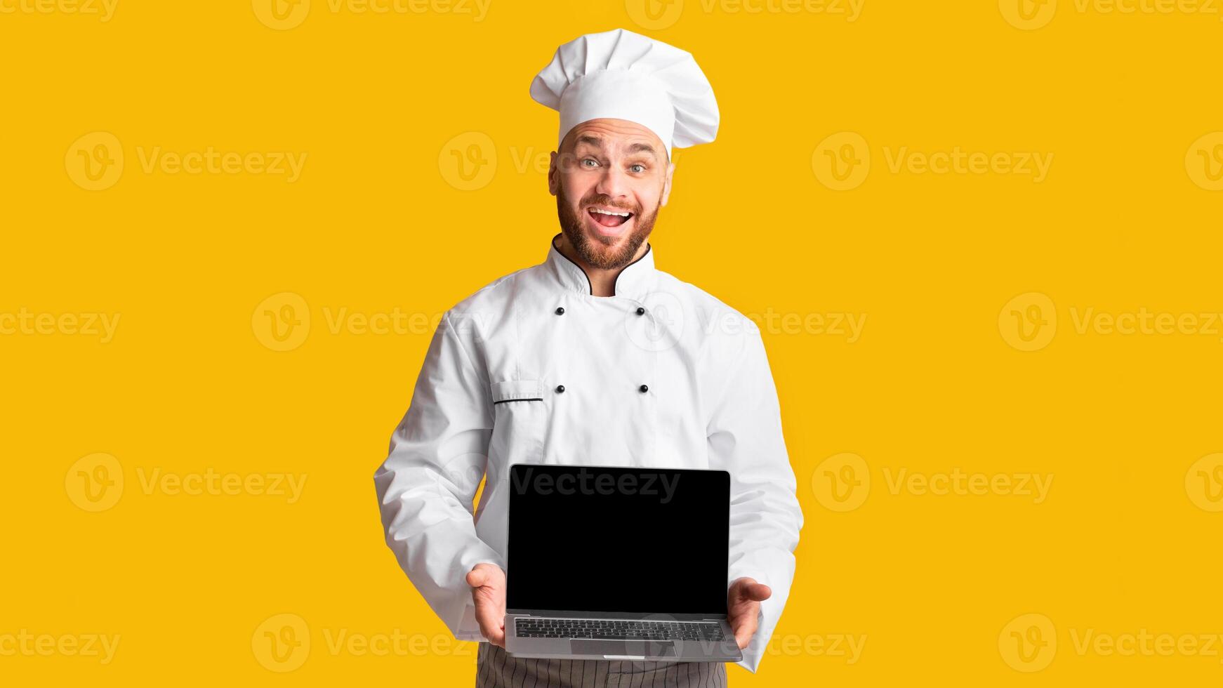 Cooking Food Website. Happy Chef Man Holding Laptop Computer Showing Blank Screen Posing On Yellow Background. Studio Shot photo
