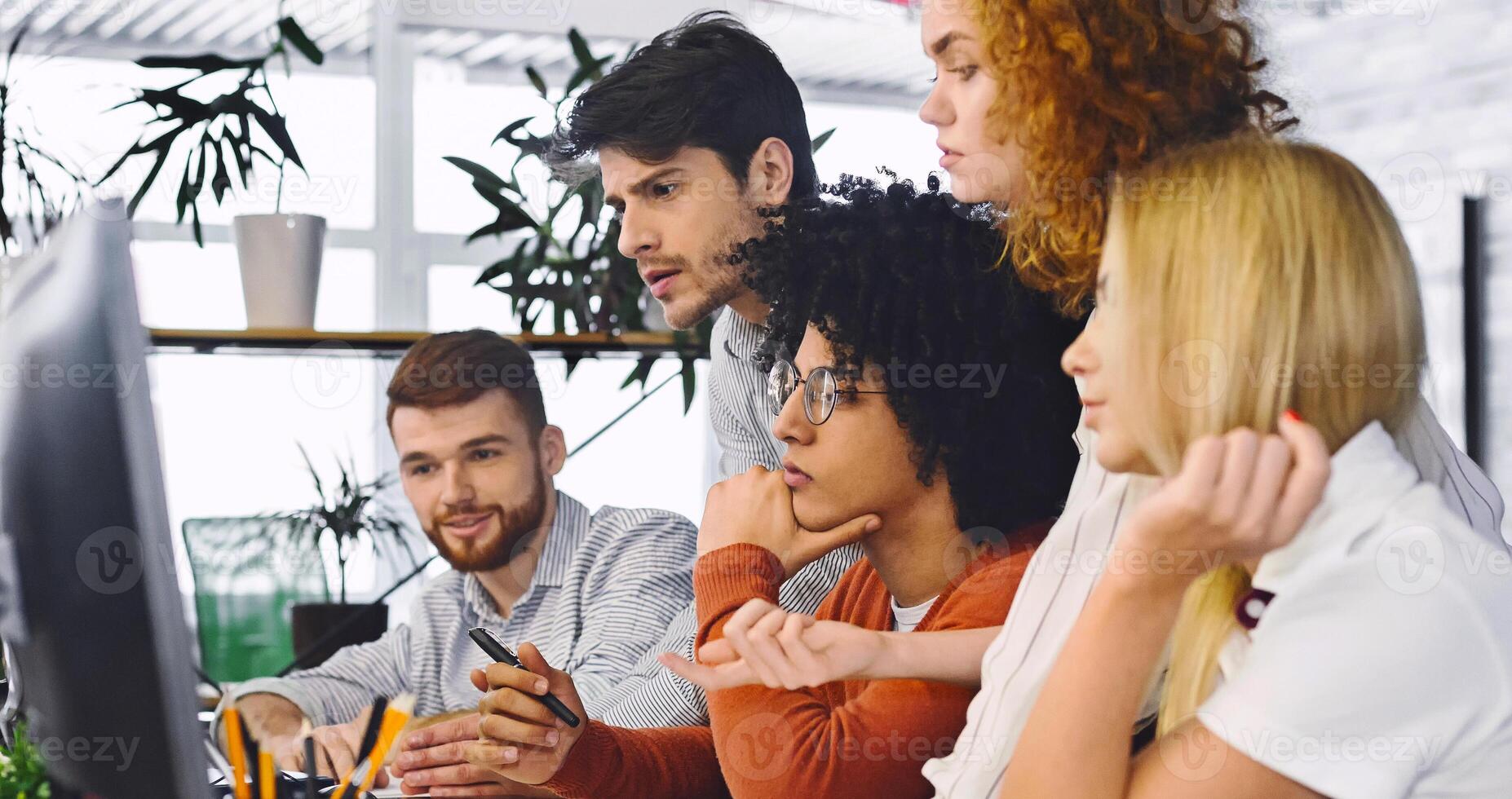 Collective brainstorm. Pensive millennial team reading business information on computer in office, panorama photo