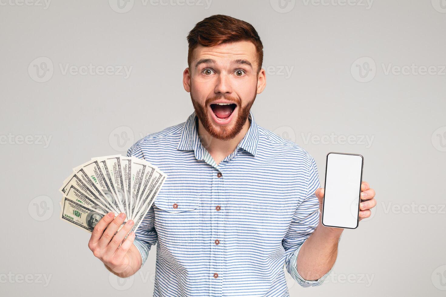 Happy to be reach. Surprised millennial guy with money and cellphone on studio background, blank space, mockup photo
