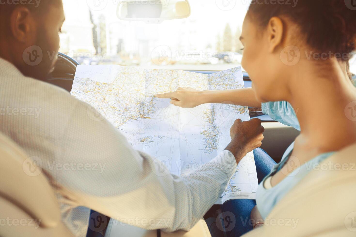African American couple sits inside a car, planning their road trip using a traditional paper map. The woman points out a location on the map to the man. photo
