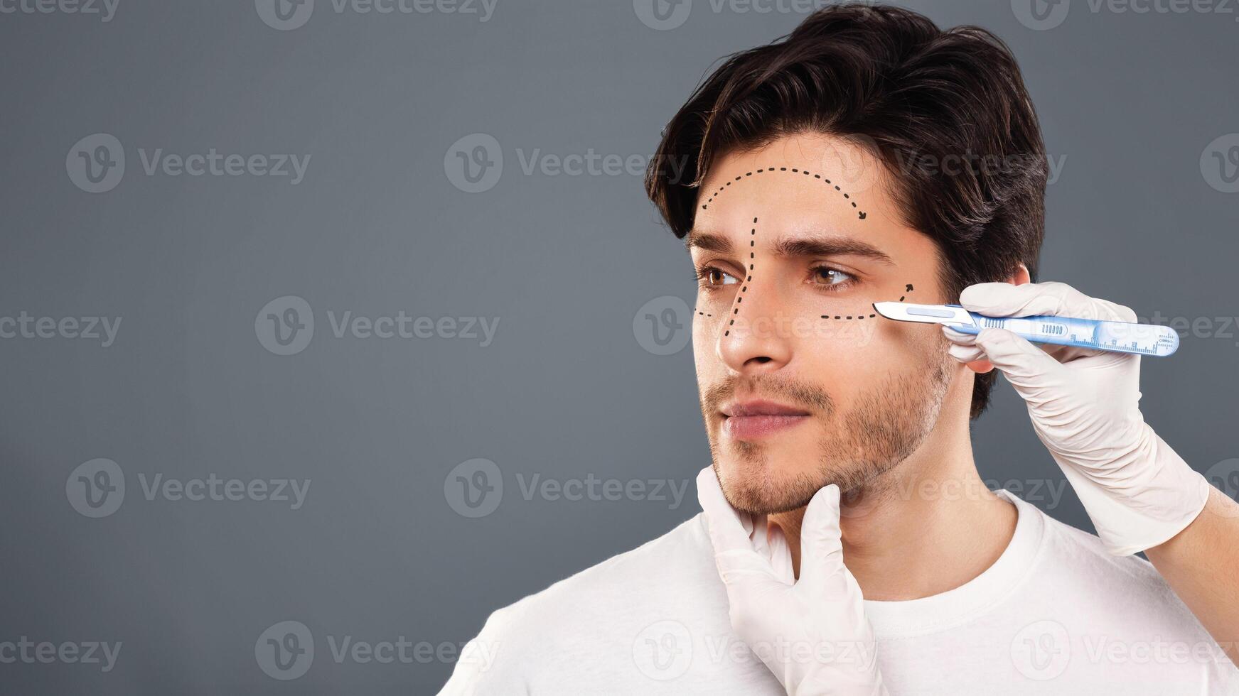 Plastic Surgery. Handsome male face with black marks on skin under eye, doctor hand with scalpel ready for operation on eyelids, free space photo