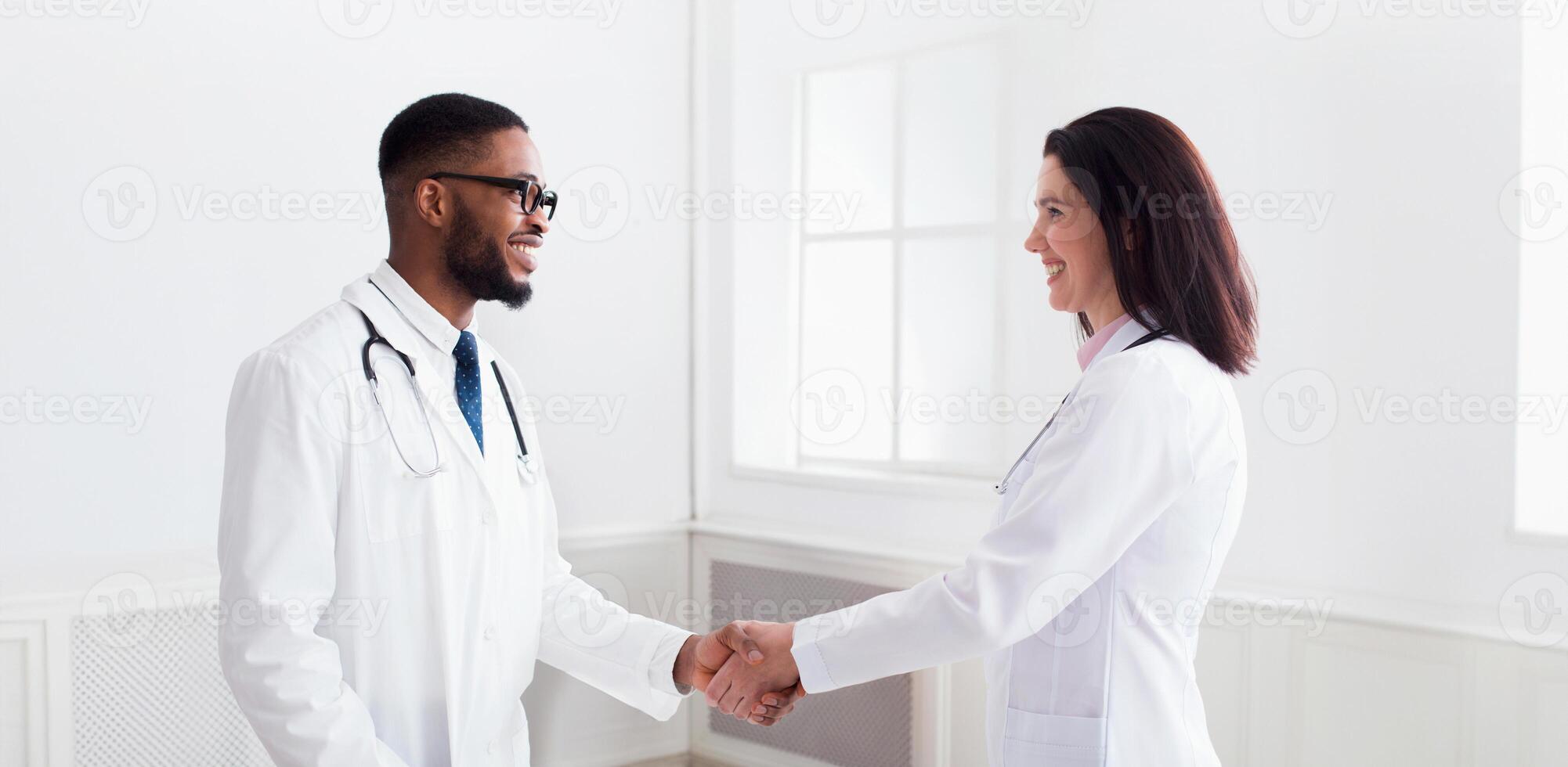 Doctor handshaking with african-american intern after meeting in clinic photo
