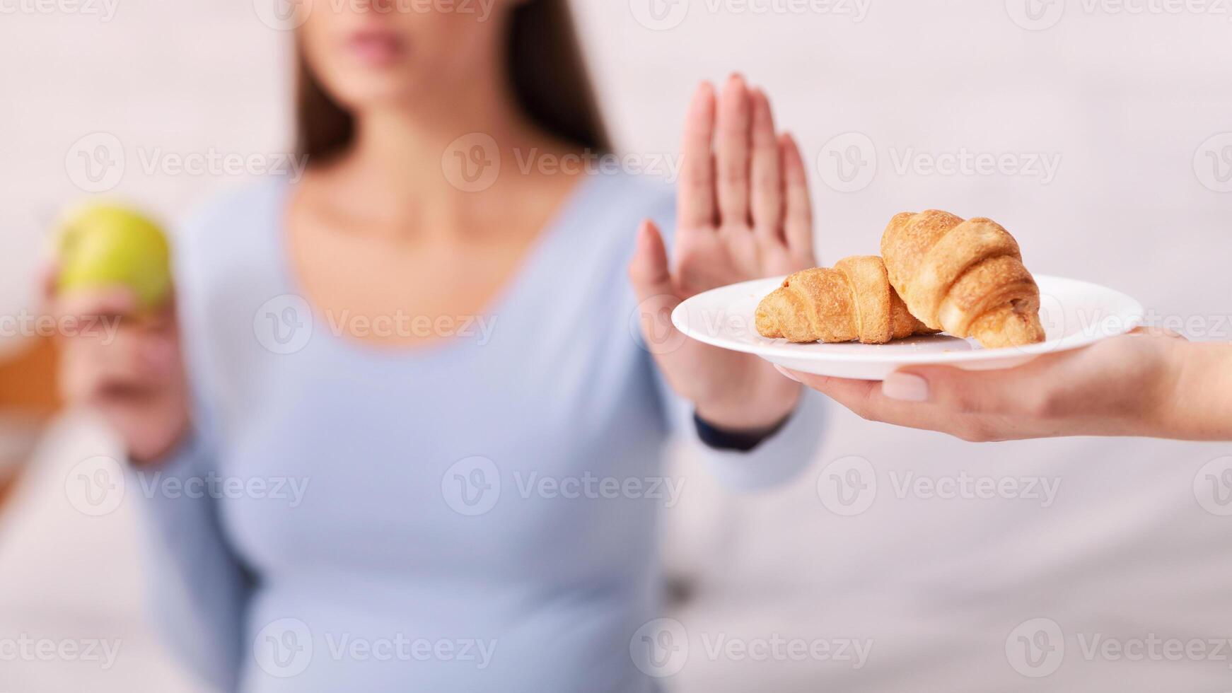 No Pastry During Pregnancy. Pregnant Woman Refusing To Take Unhealthy Croissants Choosing Apple Sitting On Bed Indoor. Selective Focus photo