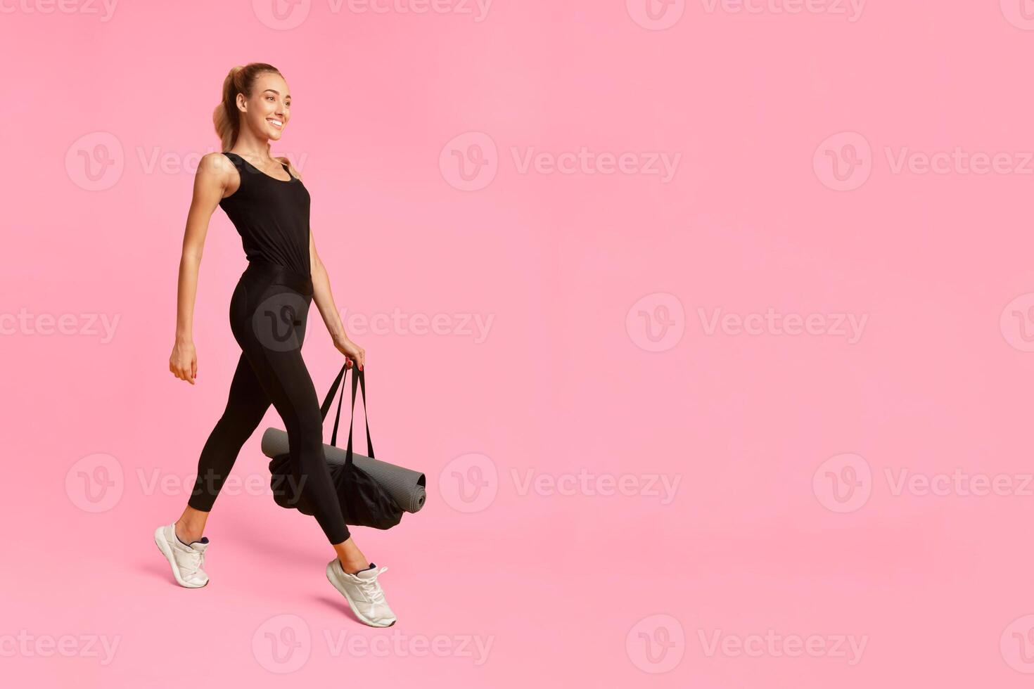 Smiling Fitness Lady Going To Gym Carrying Bag With Rolling Mat On Yellow Studio Background. Full Length photo