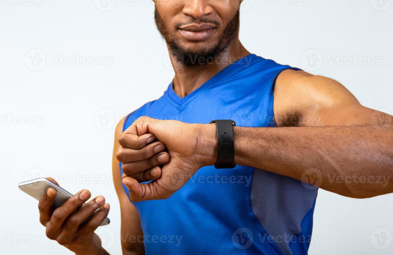 Fitness Tracker. Portrait of afro muscular man holding mobile phone and looking at smartwatch, yellow wall, copyspace photo