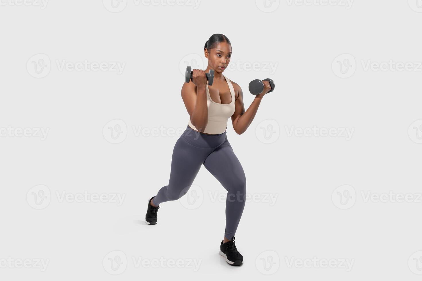 Black woman is standing on a white background, lifting dumbbells with both hands. She is focused and determined, showcasing strength and endurance during her workout routine. photo