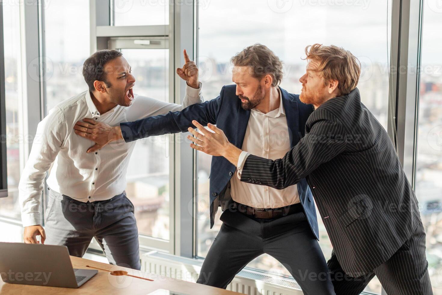 Three men in suits are engaged in a heated argument in a modern office setting. The man in the white shirt is yelling at the man in the blue suit, who is pushing him away photo