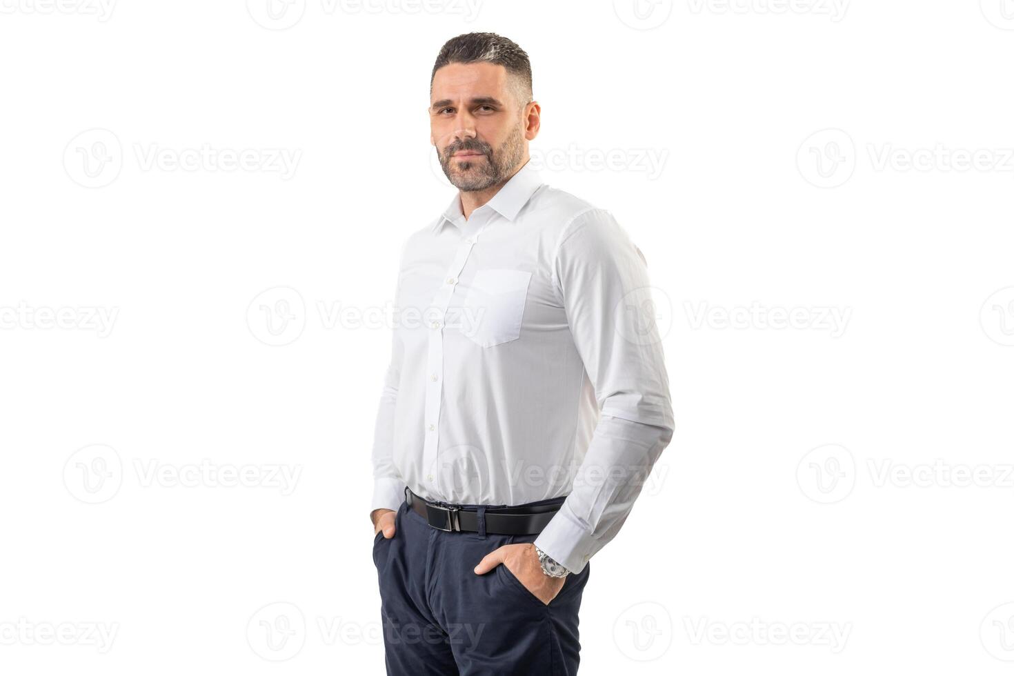 A confident man with neatly groomed hair and a trimmed beard is standing with his hands in his pockets. He is dressed in a white shirt and blue pants, exuding a professional and approachable demeanor. photo