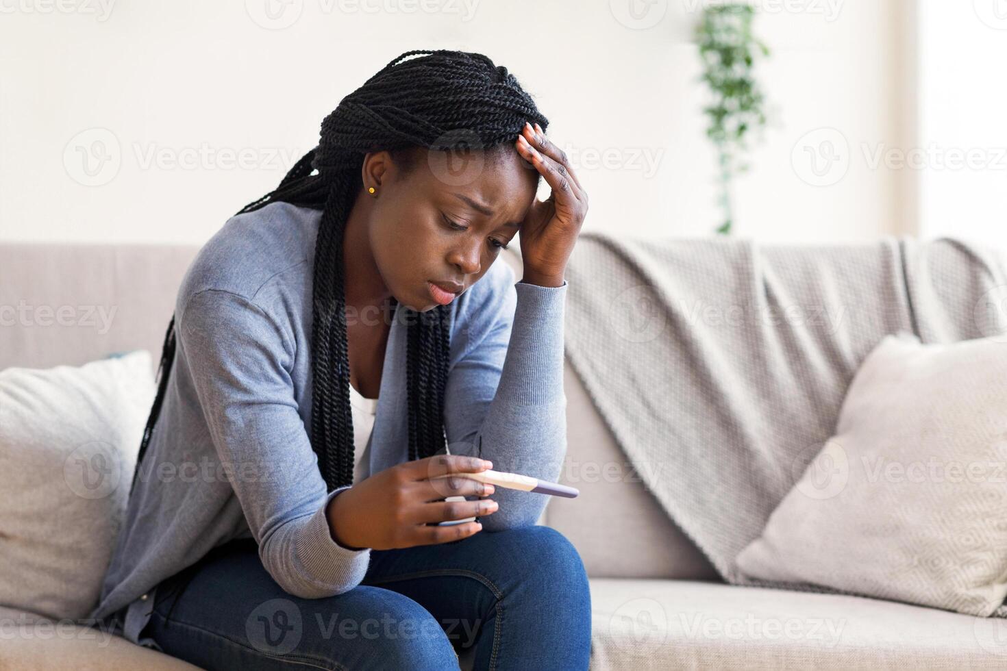Unintended pregnancy. Depressed african american woman upset with positive test results, sitting on couch at home with sad face expression photo