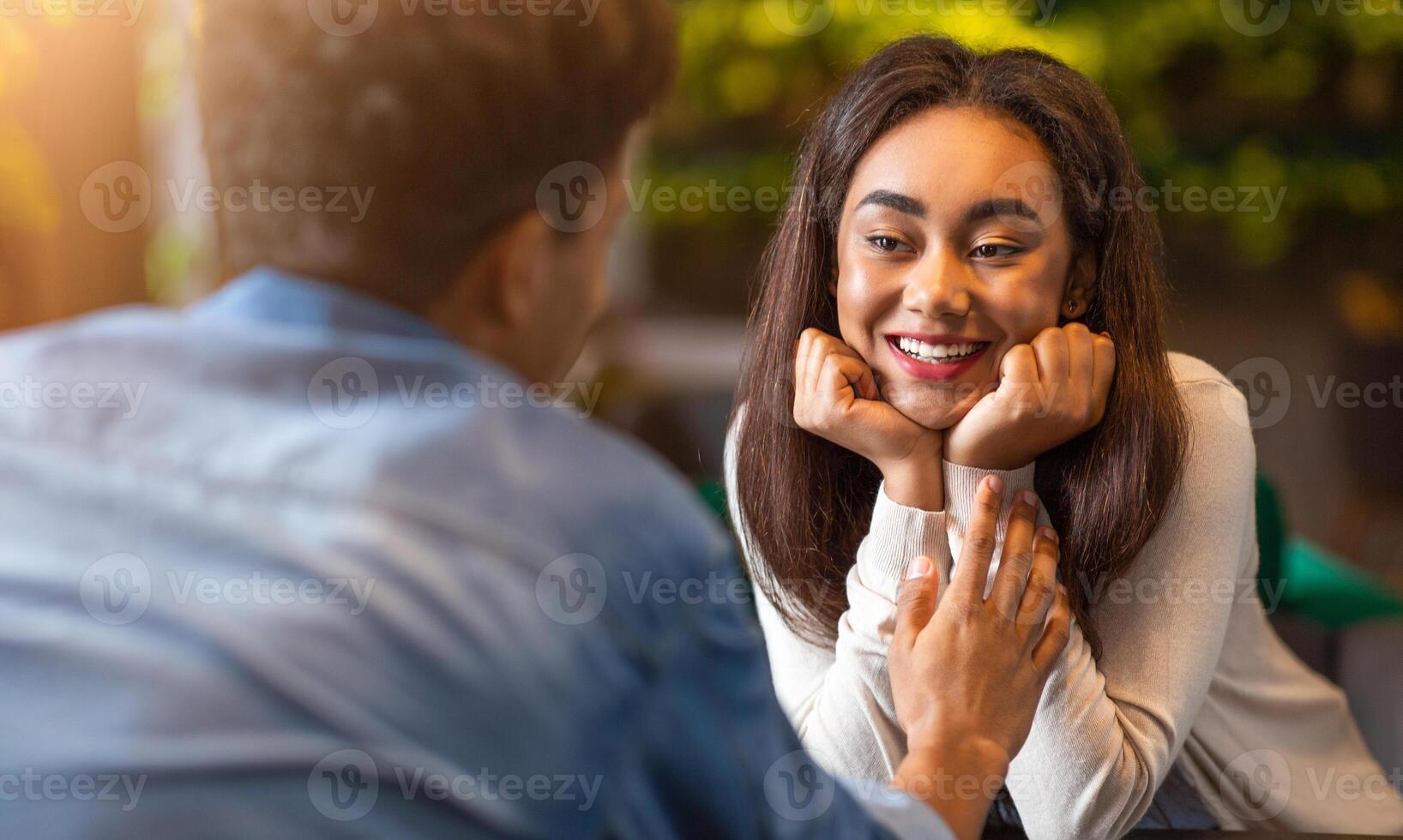 African American guy and girl are engaged in conversation at a table in a restaurant. Both individuals appear to be attentive to each other, leaning in slightly as they speak. photo