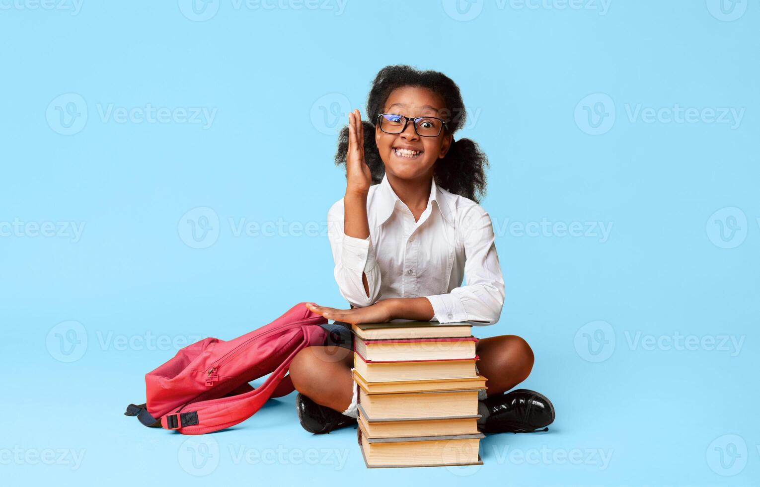 Clever Black Elementary School Girl Raising Hand Sitting At Book Stack Over Yellow Background In Studio. Free Space photo