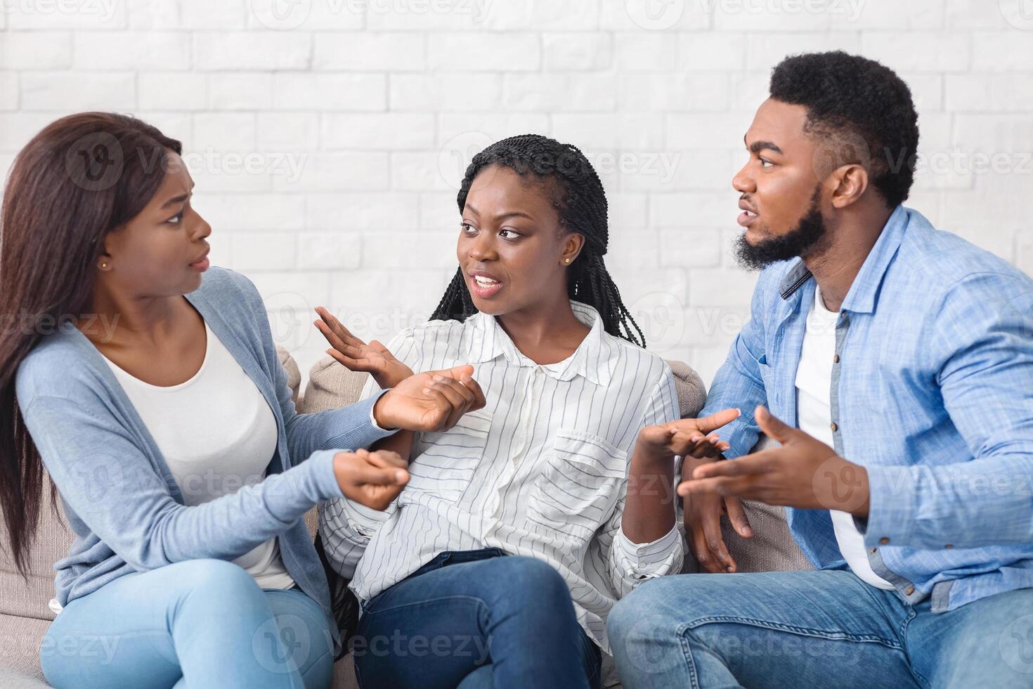 Upset black woman trying to stop friends from quarreling, sitting between them and actively gesturing, copy space photo