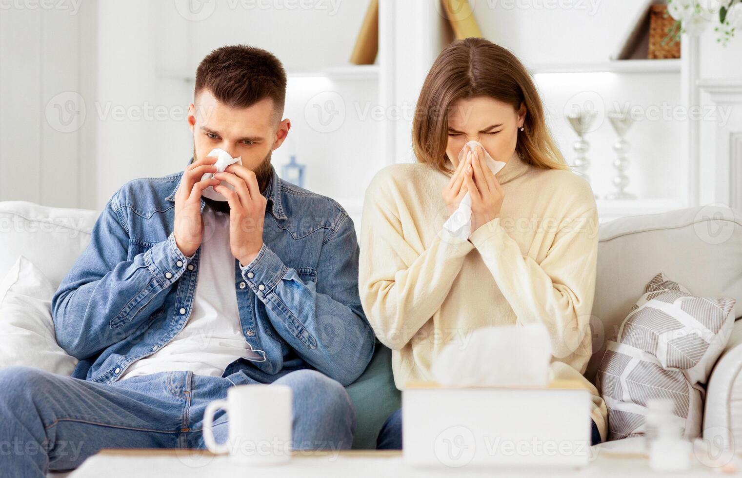 Couple Suffering From Cold, Blowing Noses And Sneezing, Sitting On Sofa At Home photo