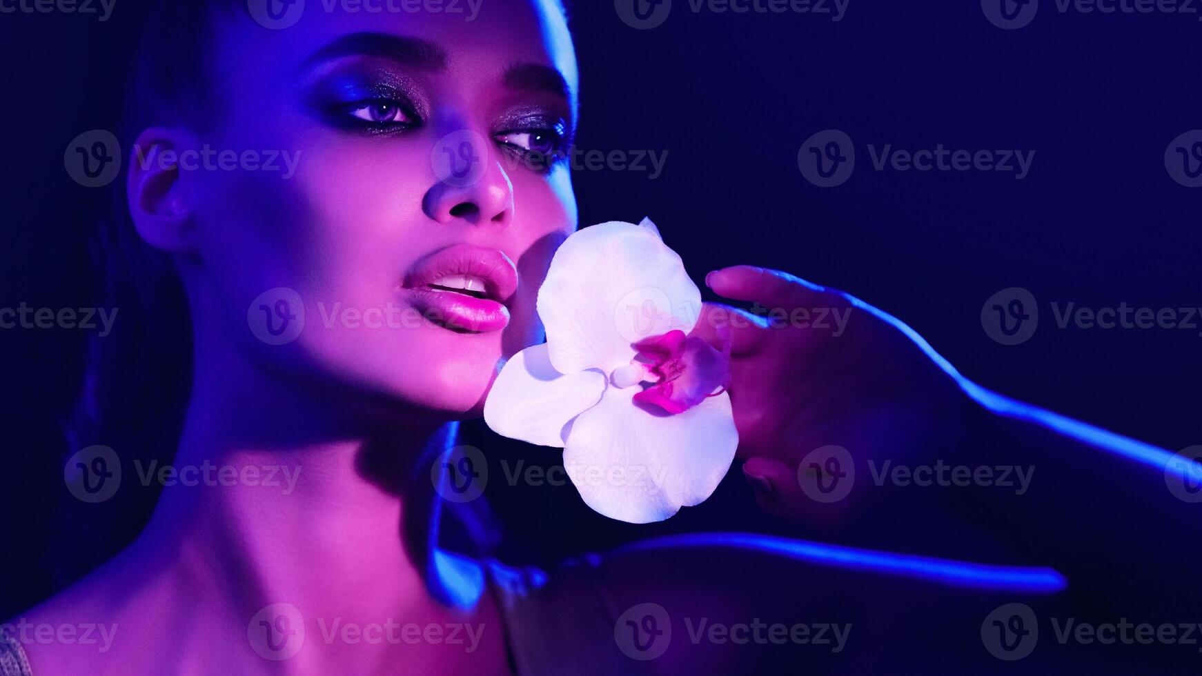 A woman is standing while holding a delicate flower in her hand. She appears focused on the bloom, showcasing its intricate details. photo