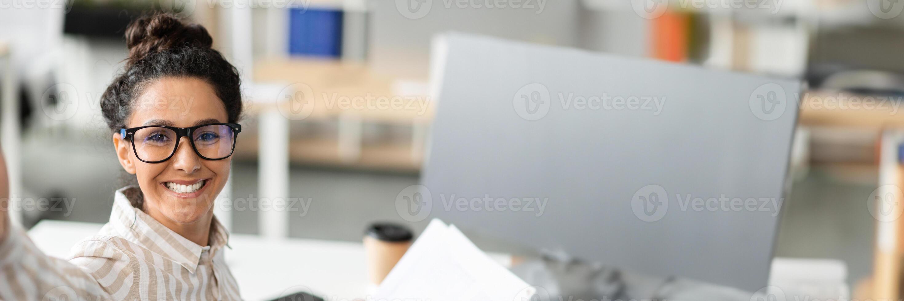 Happy businesswoman having call or taking selfie while working with documents in office and smiling at camera. Confident lady entrepreneur communicating online at workplace, copy space photo