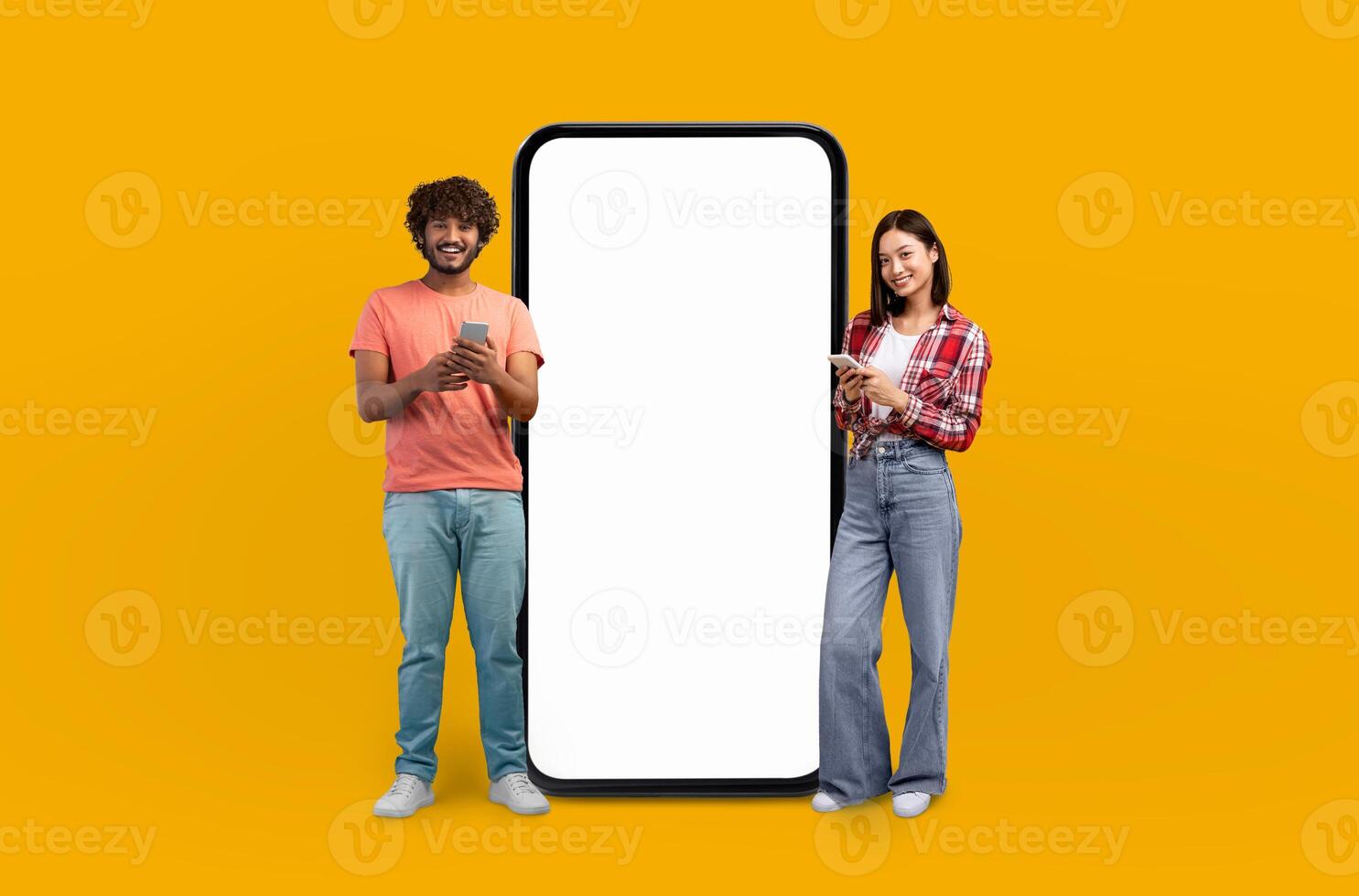 The vibrant yellow background highlights the smiling multiethnic young adults as they gesture towards the expansive blank screen of the smartphone beside them. photo
