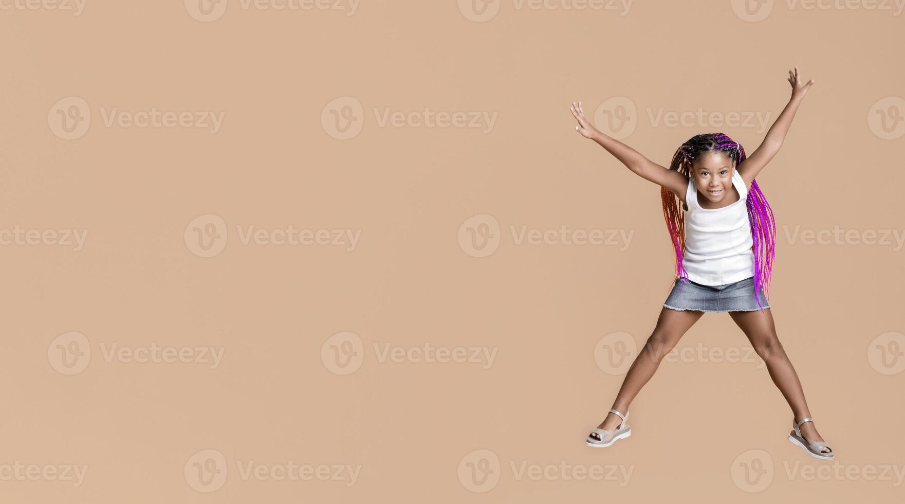 Like a star. Cute little african american girl jumping with her hands up over yellow studio background with copy space photo