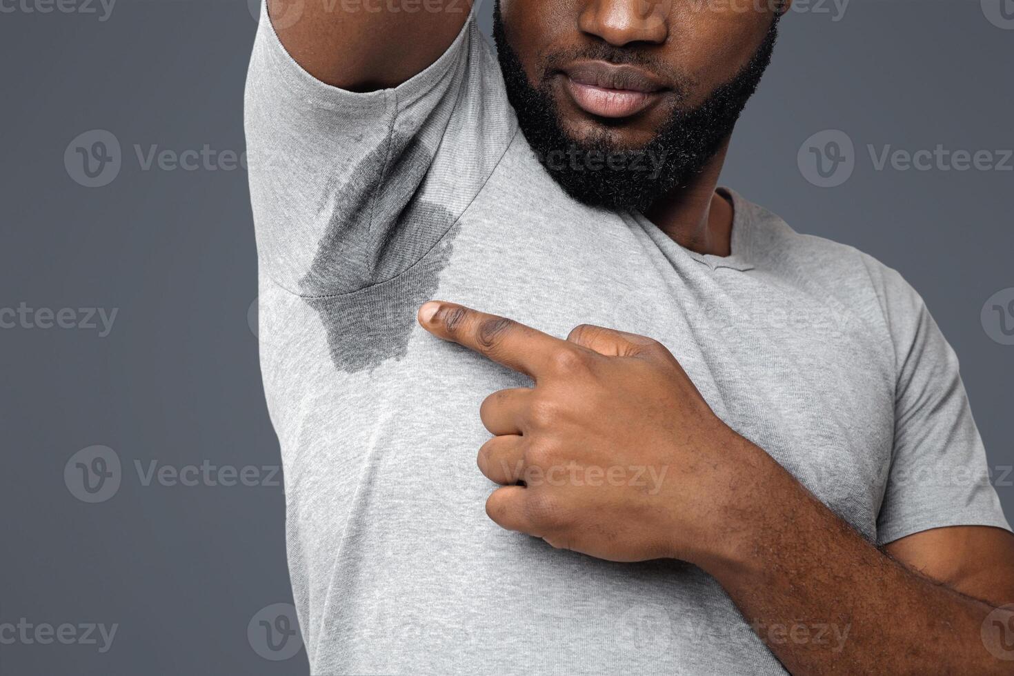 Cropped of young afro man looking at the sweaty shirt, white background, copy space, wet armpit problem photo