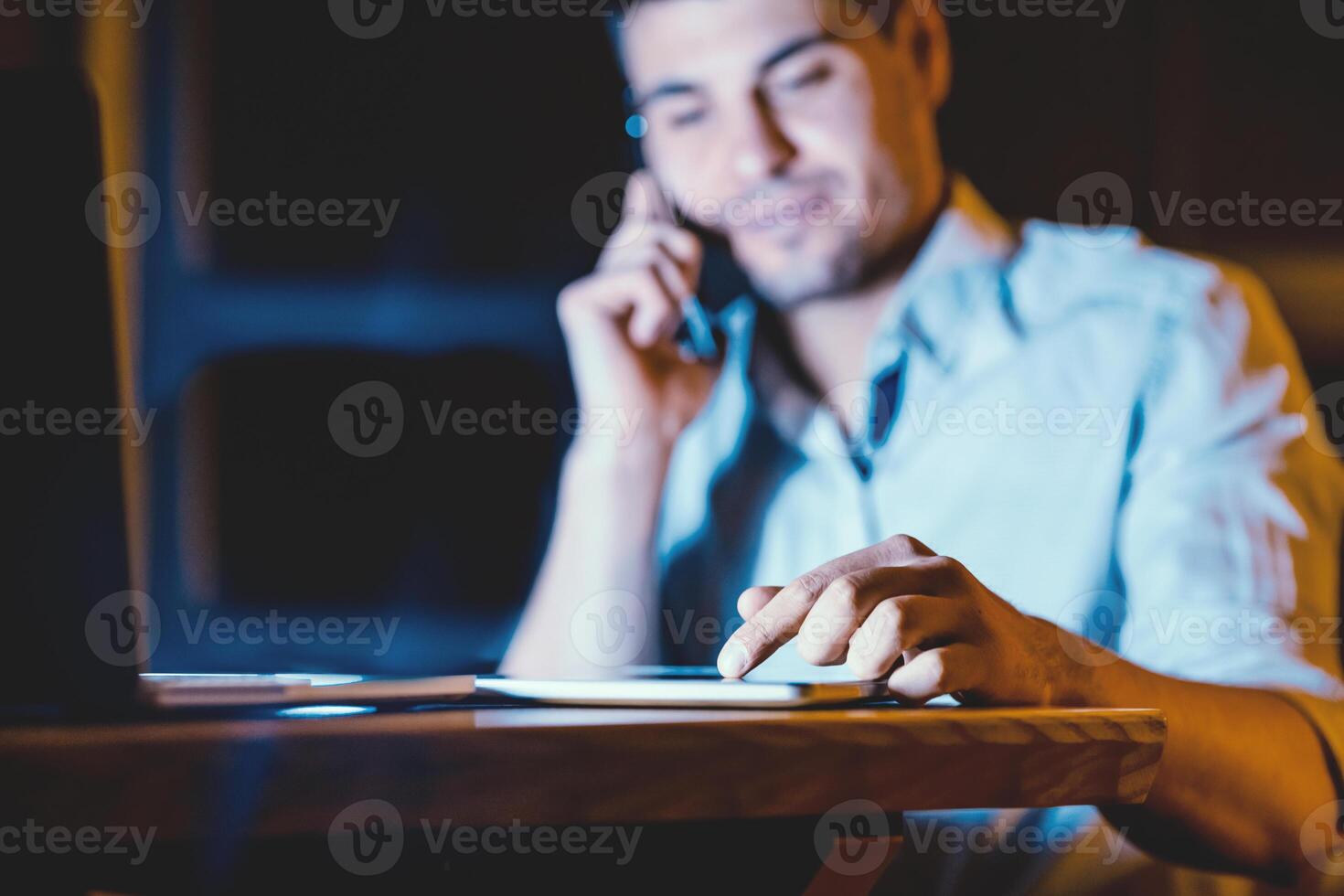 Unrecognizable Businessman Using Digital Tablet And Business Application Talking On Cellphone Working Indoors At Night. Selective Focus photo