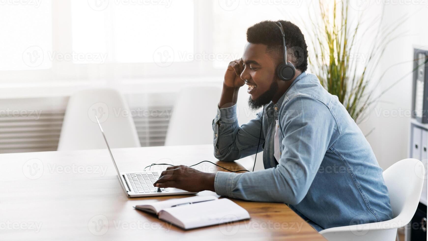 Customer support concept. Black millennial manager with headset using laptop in office, solving client's issue. photo