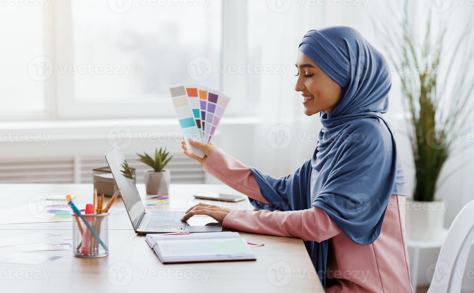 Muslim Female Graphic Designer Working With Color Swatches And Laptop In Modern Office, Choosing Palette For New Project, Side View With Free Space photo