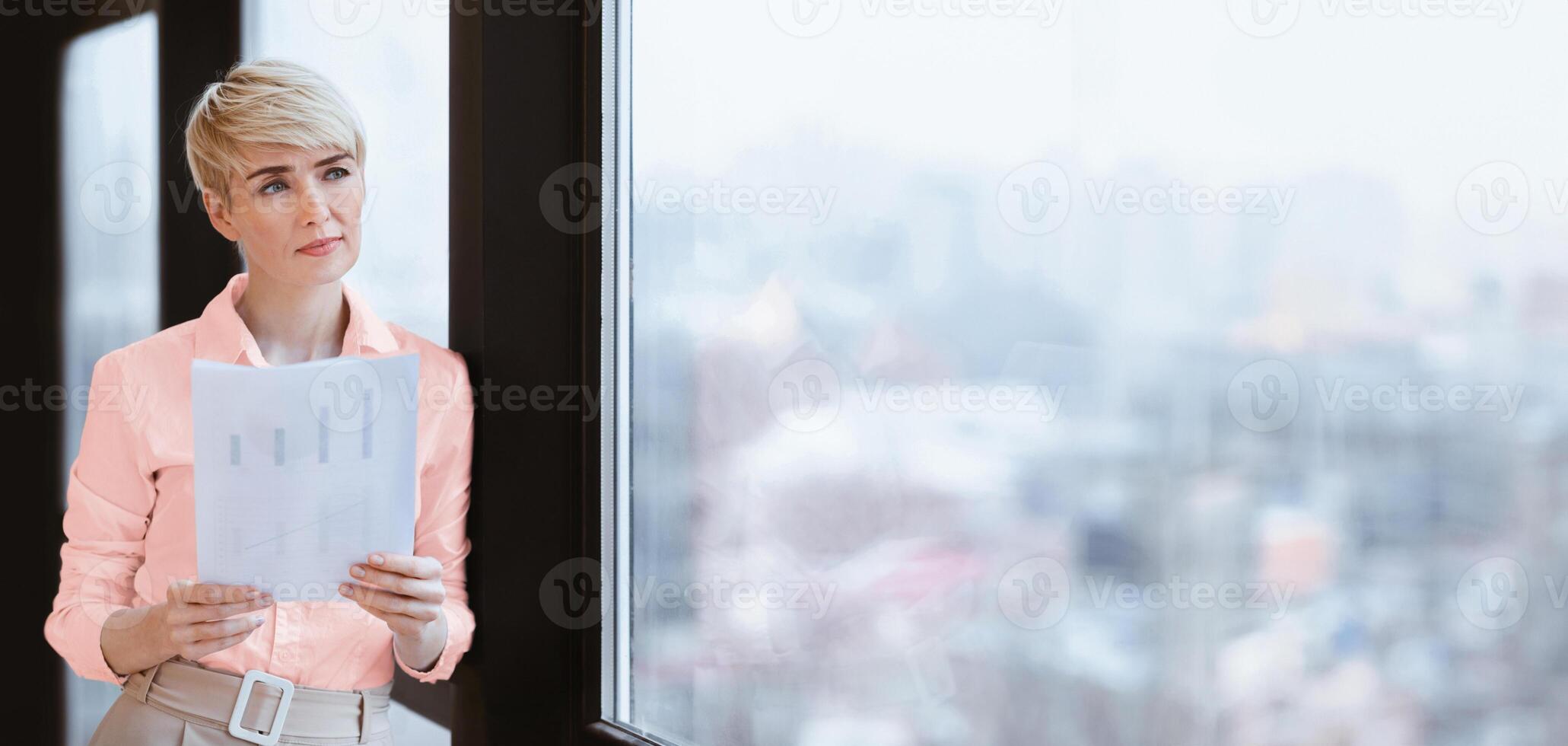 Mature Businesswoman Holding Business Report Standing Near Window In Modern Office. Successful Career. Free Space photo