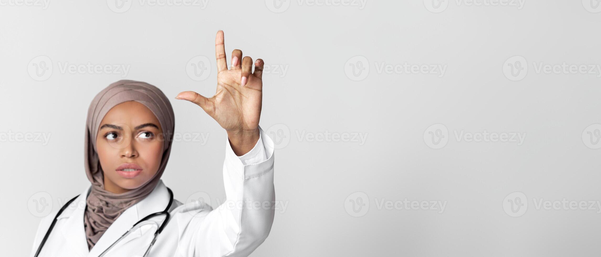 Flu Remedy Or Vaccination Concept. Black female doctor in hijab holding invisible syringe with vaccine or pack with medicine over light background photo
