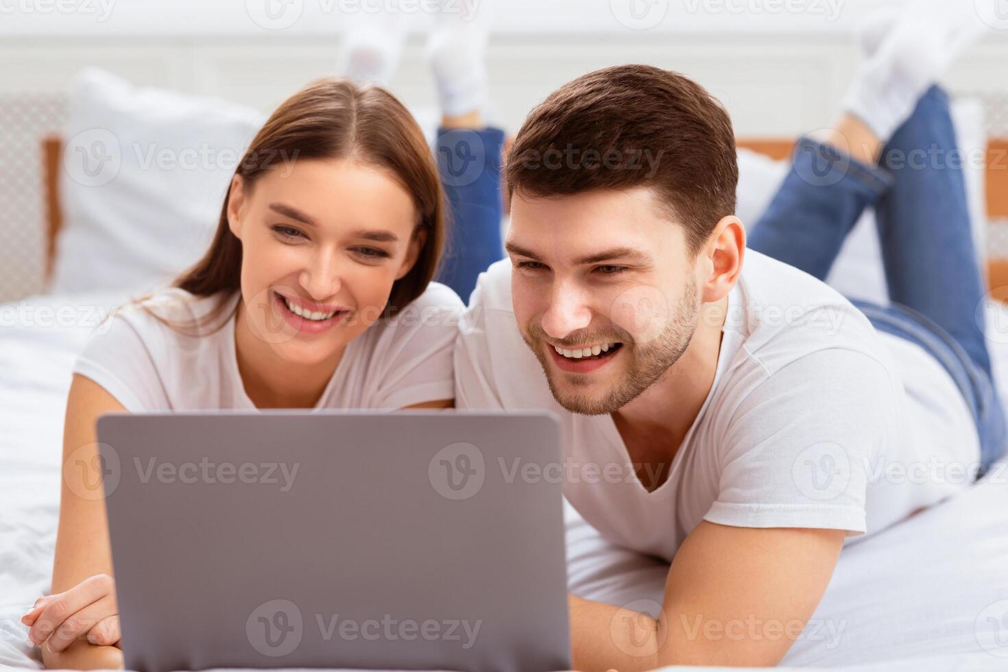 Weekend. Millennial Couple Using Laptop Lying In Bed Watching Movie Spending Weekend At Home. Selective Focus photo