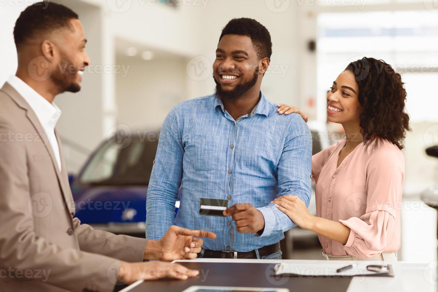 Afro Couple Buying Car Giving Seller Credit Card Standing In Auto Dealership Office. Selective Focus photo