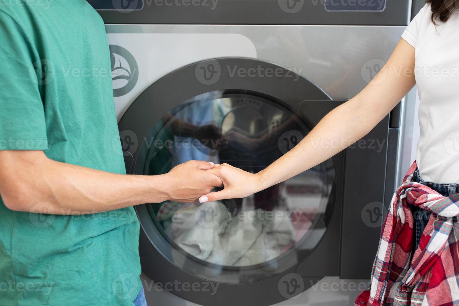 A couple is engaged in a shared moment while doing laundry at home. They hold hands near the washing machine, enjoying each other company amidst household chores, cropped photo