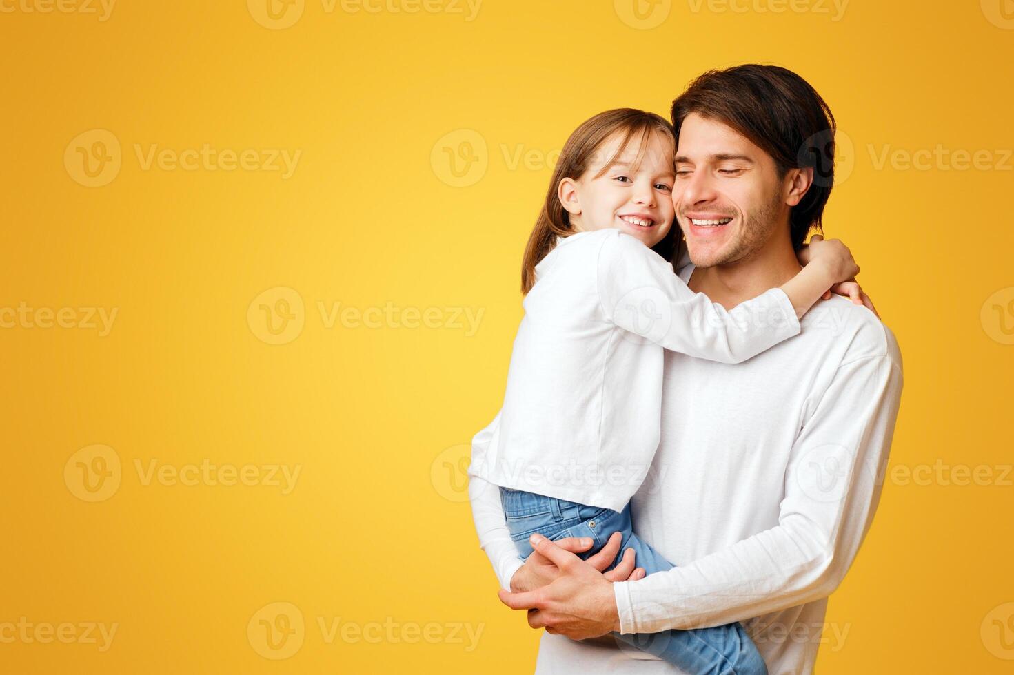 Positive father and little daughter posing together on yellow background, dad holding girl, daughter hugging father, free space photo