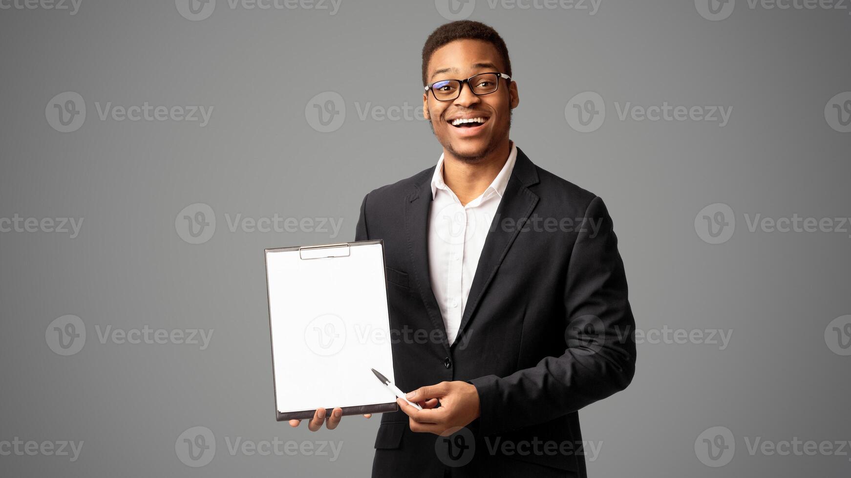 Sign Here. Happy afro man pointing at blank clipboard with pen, doing survey. Empty space, panorama, white studio photo