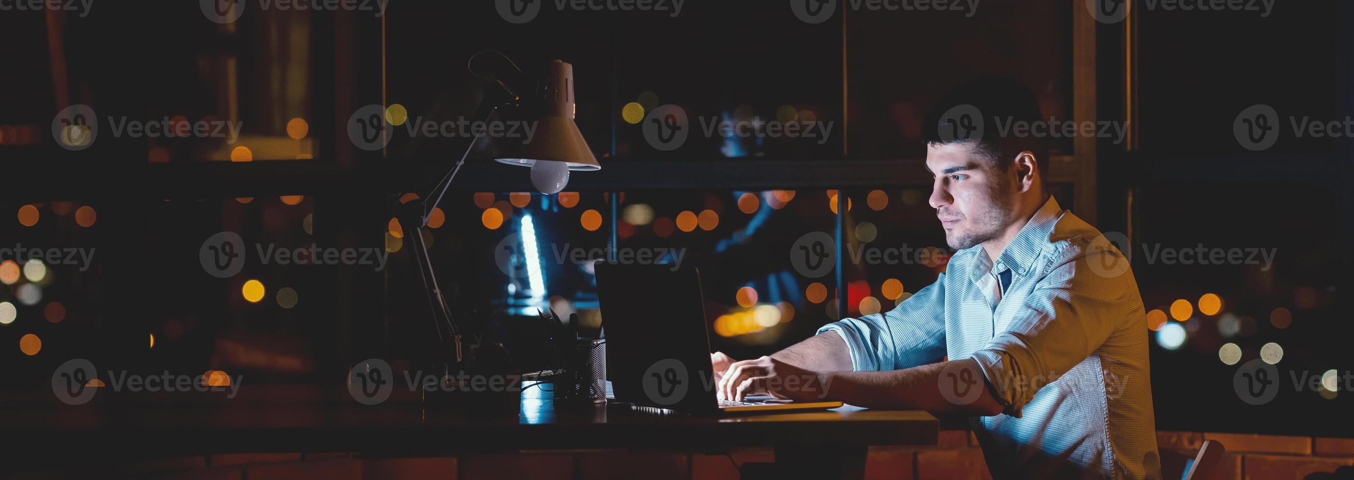 Business Career. Young Businessman At Laptop Working Overtime Sitting Near Window With Night City View In Modern Office. Free Space photo