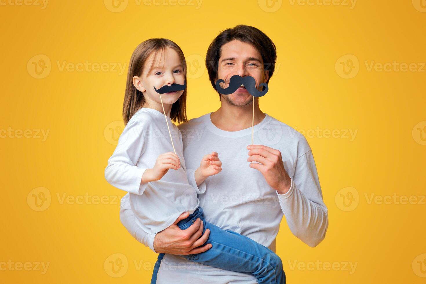Funny little girl and daddy have mustaches on sticks, posing over yellow background photo