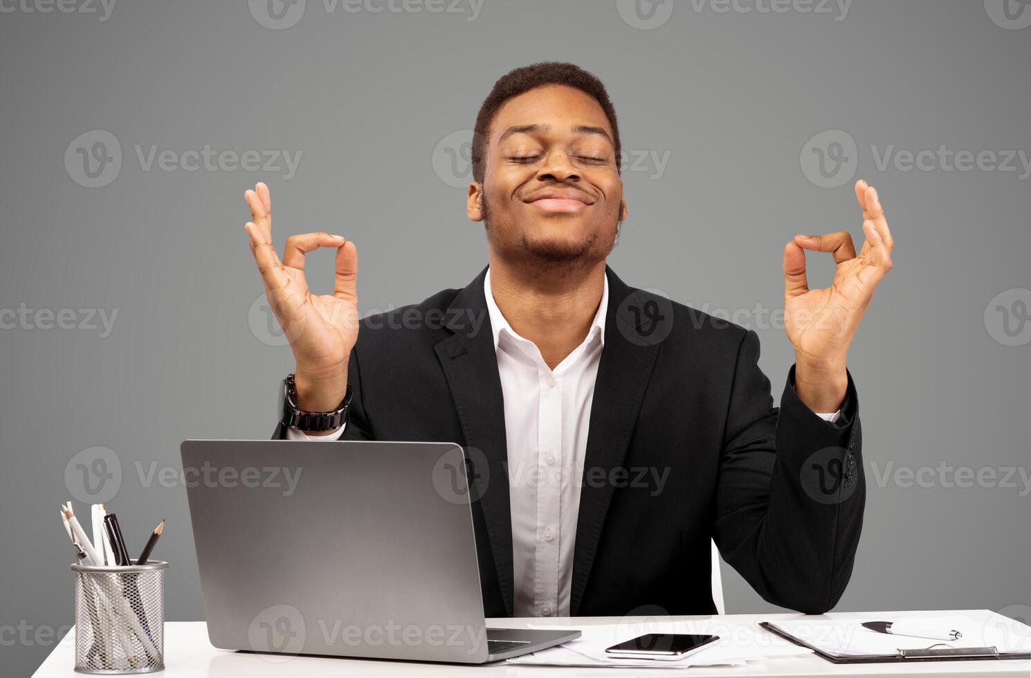 Stress Management. Afro businessman meditating, working on laptop, missing deadline. White studio wall, free space photo
