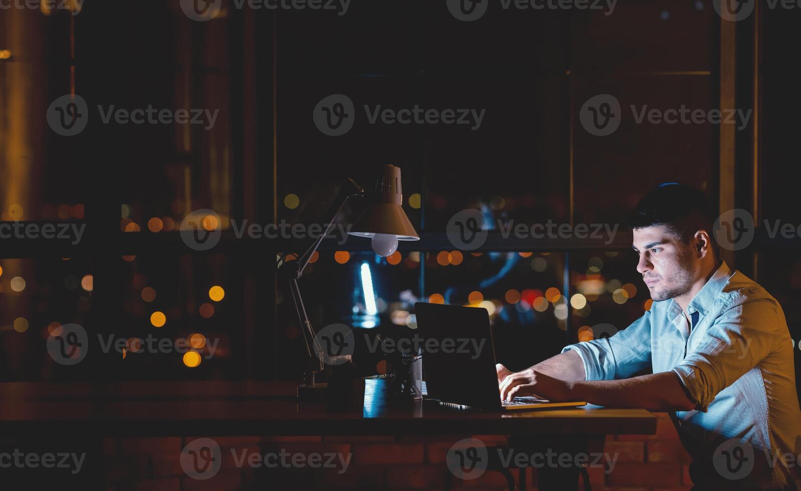 Entrepreneur Guy Working On Laptop Creating Business Startup Overnight Sitting In Modern Office Near Panoramic Window. Free Space For Text photo