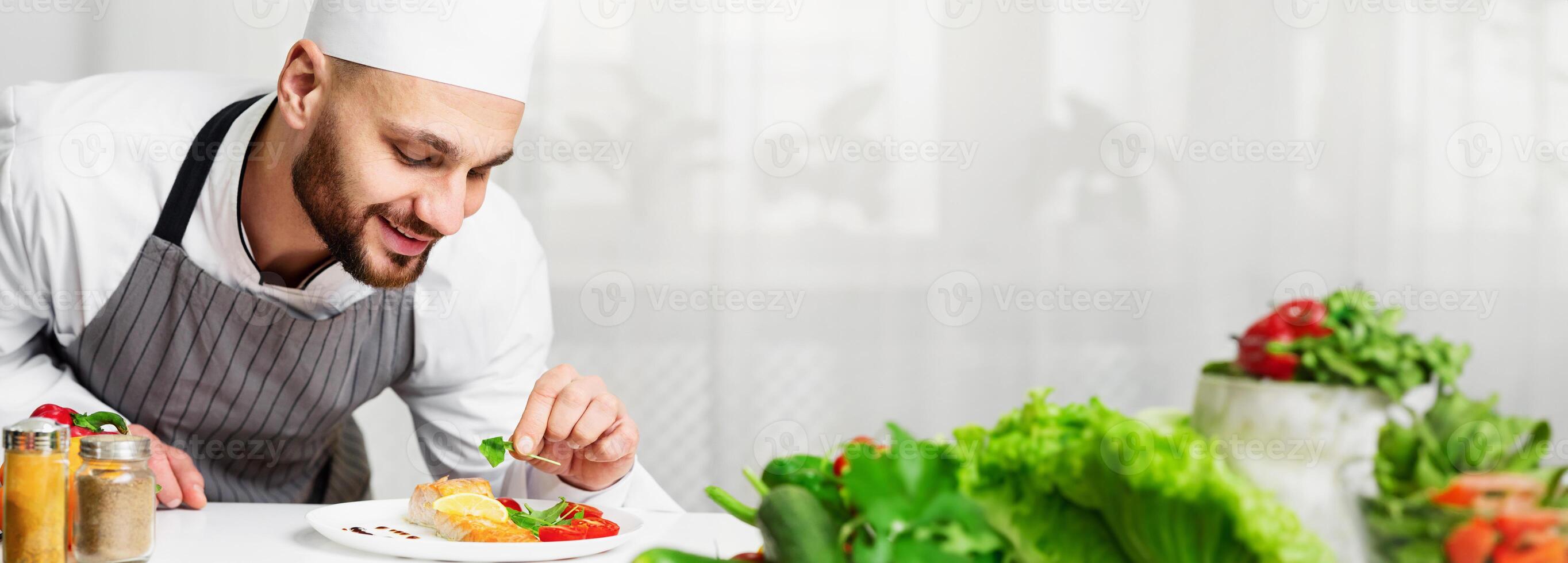 Cooking Fish. Happy Chef Guy Plating Roasted Salmon Steak And Decorating Dish With Herbs In Kitchen. Selective Focus photo