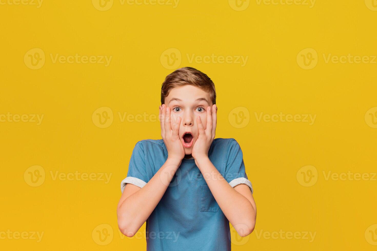 Surprised little boy. Shocked kid keeping mouth open and touching face, orange studio background photo