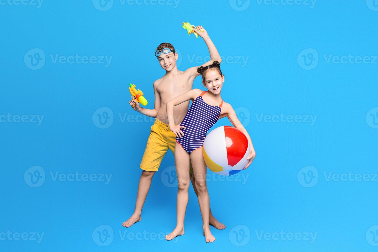 Happy summer holidays. Cheerful boy and girl playing with beach toys, blue studio background photo