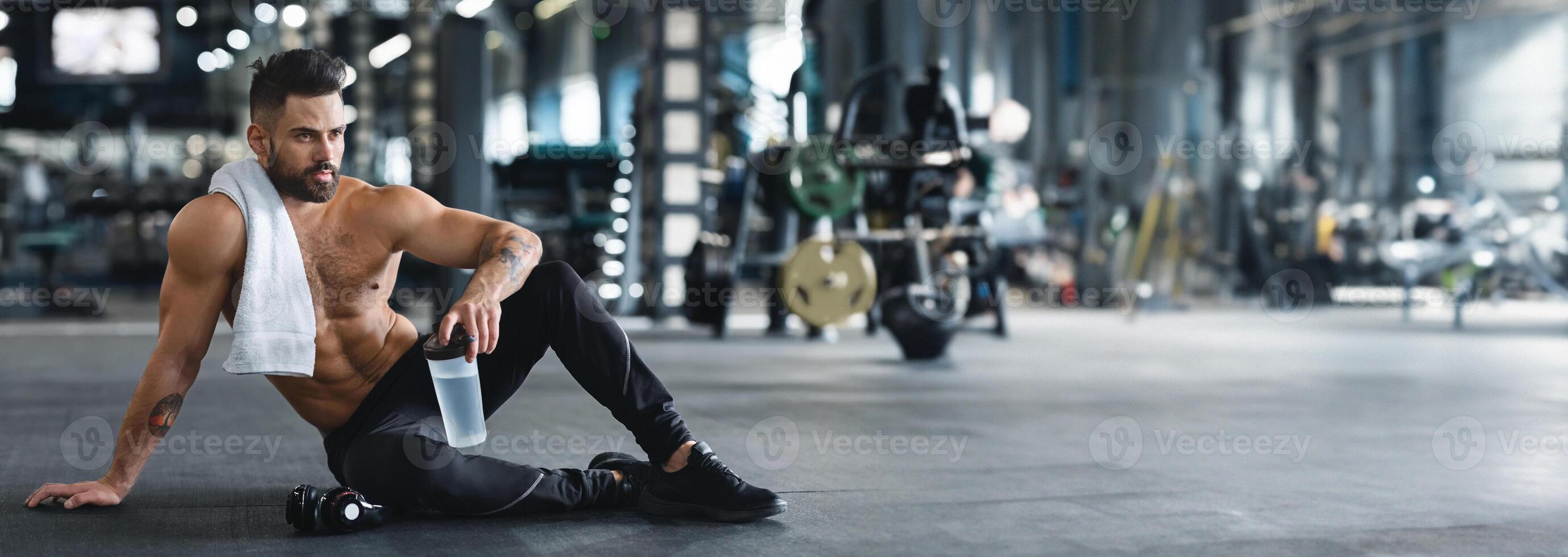 Concentrated muscular man drinking water, having break in hard workout in gym, free space, web-banner photo