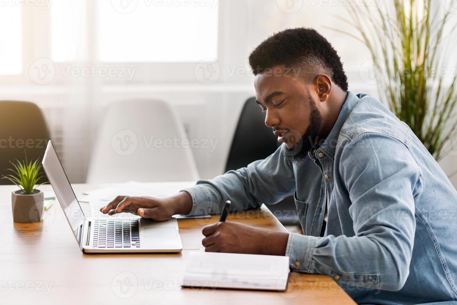 African American employee using laptop and taking notes while working in office, side view with copy space photo