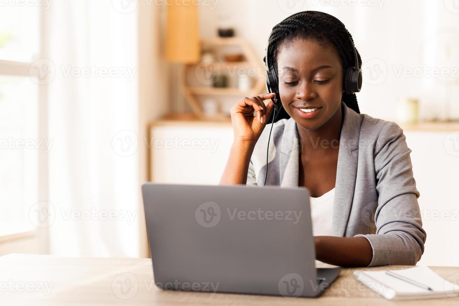 Call center operator at work. Beautiful afro female manager wearing headset and typing at laptop, consulting clients, working in modern office. photo