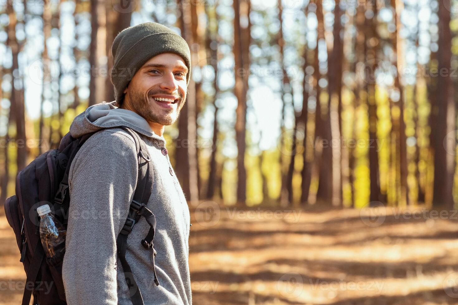 Smiling young man backpacker hiking with friends at forest, looking at camera, back view photo