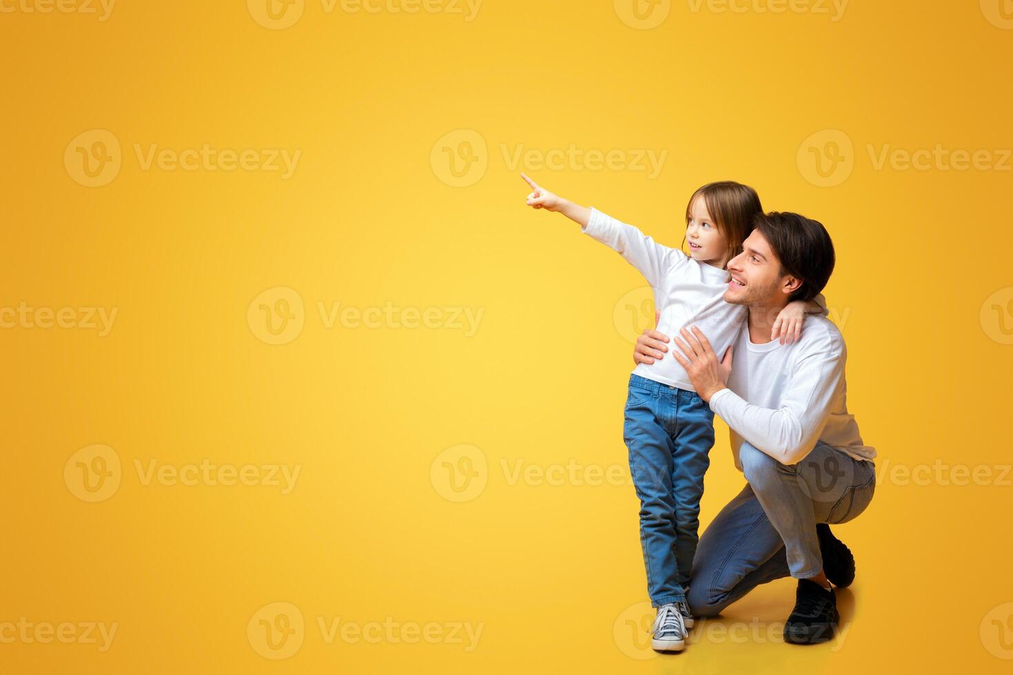 Excited cute little girl pointing her daddy at copy space over yellow background, showing nice offer, discounts for kids photo