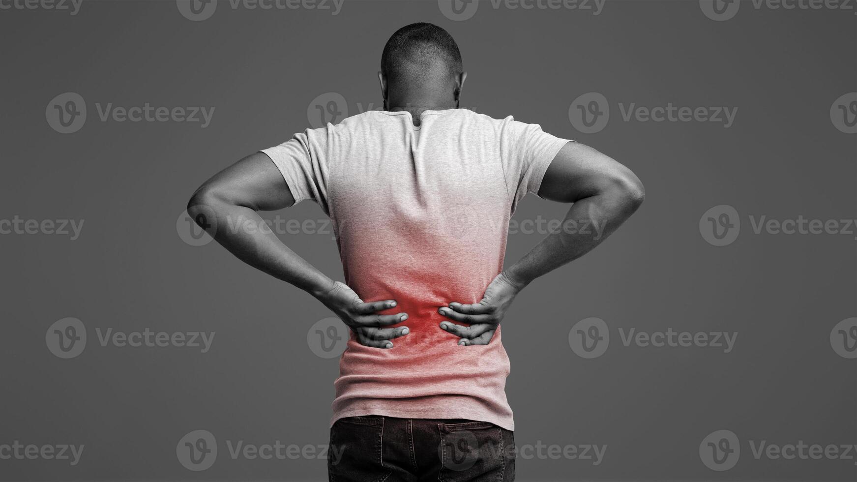 Afro guy holding both hands behind his back, pain in spine, inflamed zone highlighted in red, white background photo