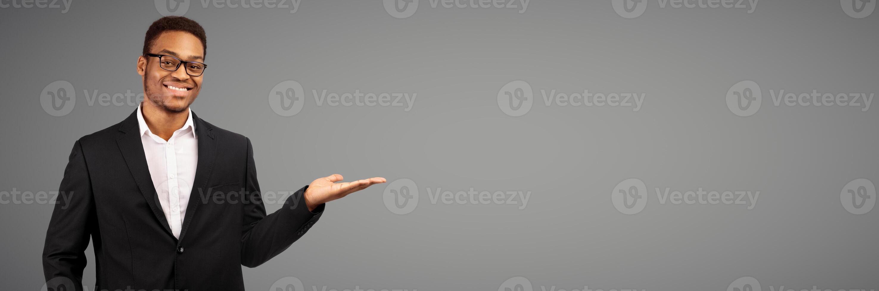 Buy This. Happy afro businessman holding invisible object on his palm, white studio wall, copyspace, panorama photo