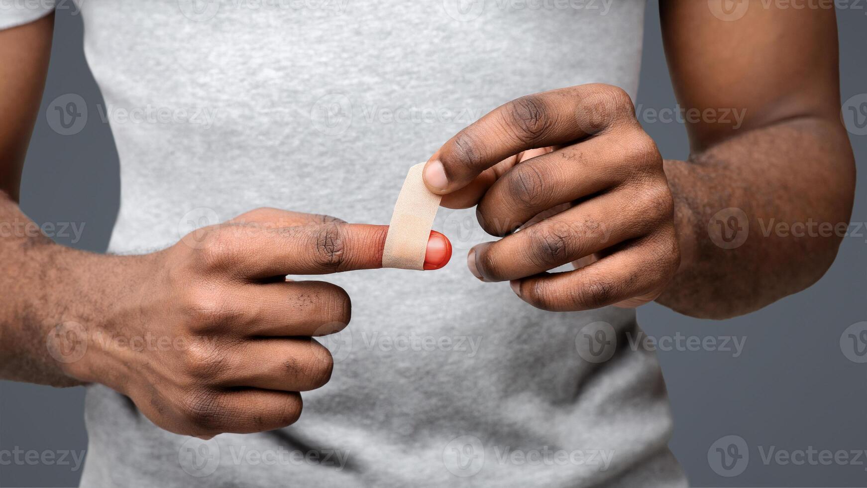 Black man using adhesive tape on injured finger, self-treatment after trauma, close up photo