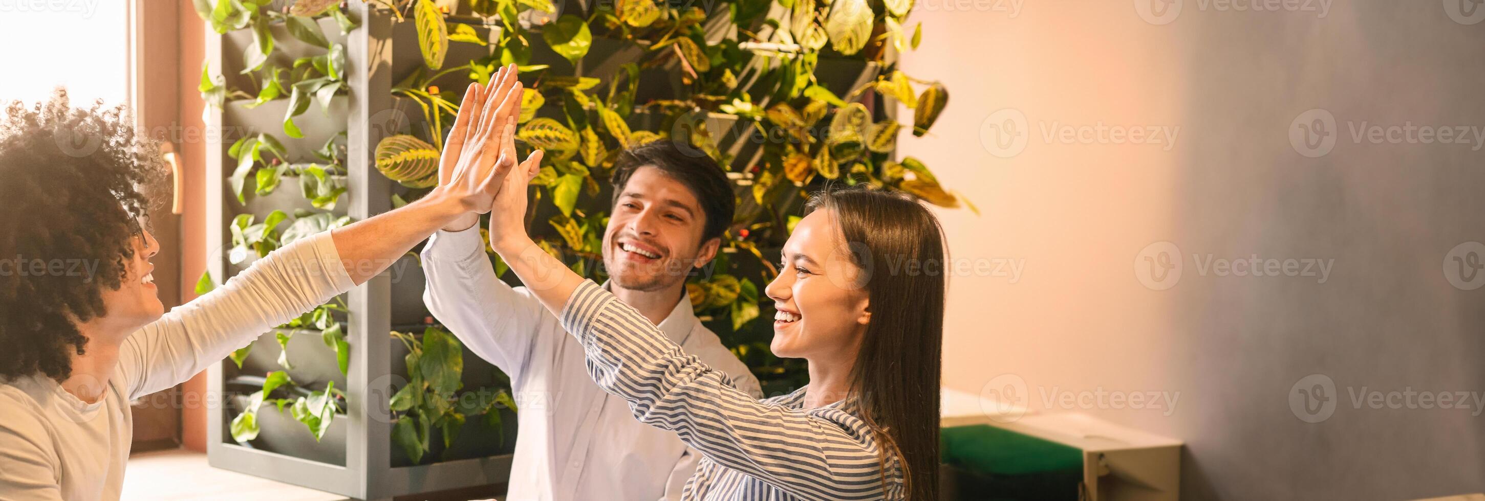 Excited multiethnic team giving each other high five, celebrating success while working together on project at cafe, copy space photo