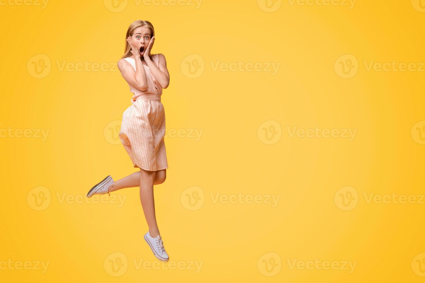 Shocking Sale. Young Woman Jumping In Air And Touching Face With Amazement, Shouting Wow With Open Mouth, Posing Over Yellow Background photo